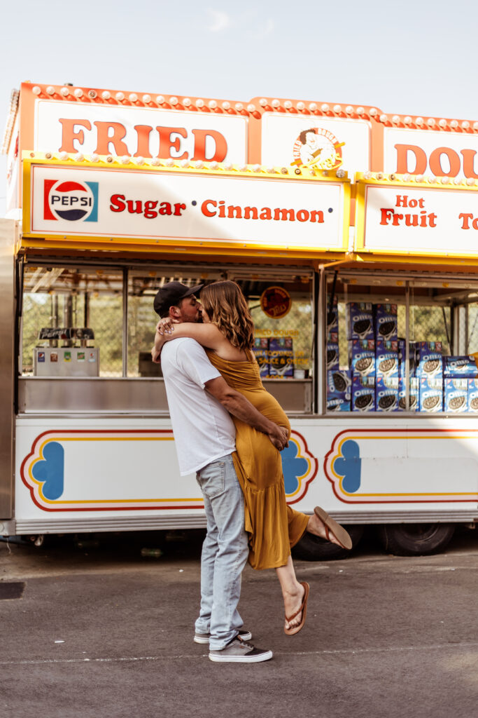 A couple kissing in front of a carnival food truck